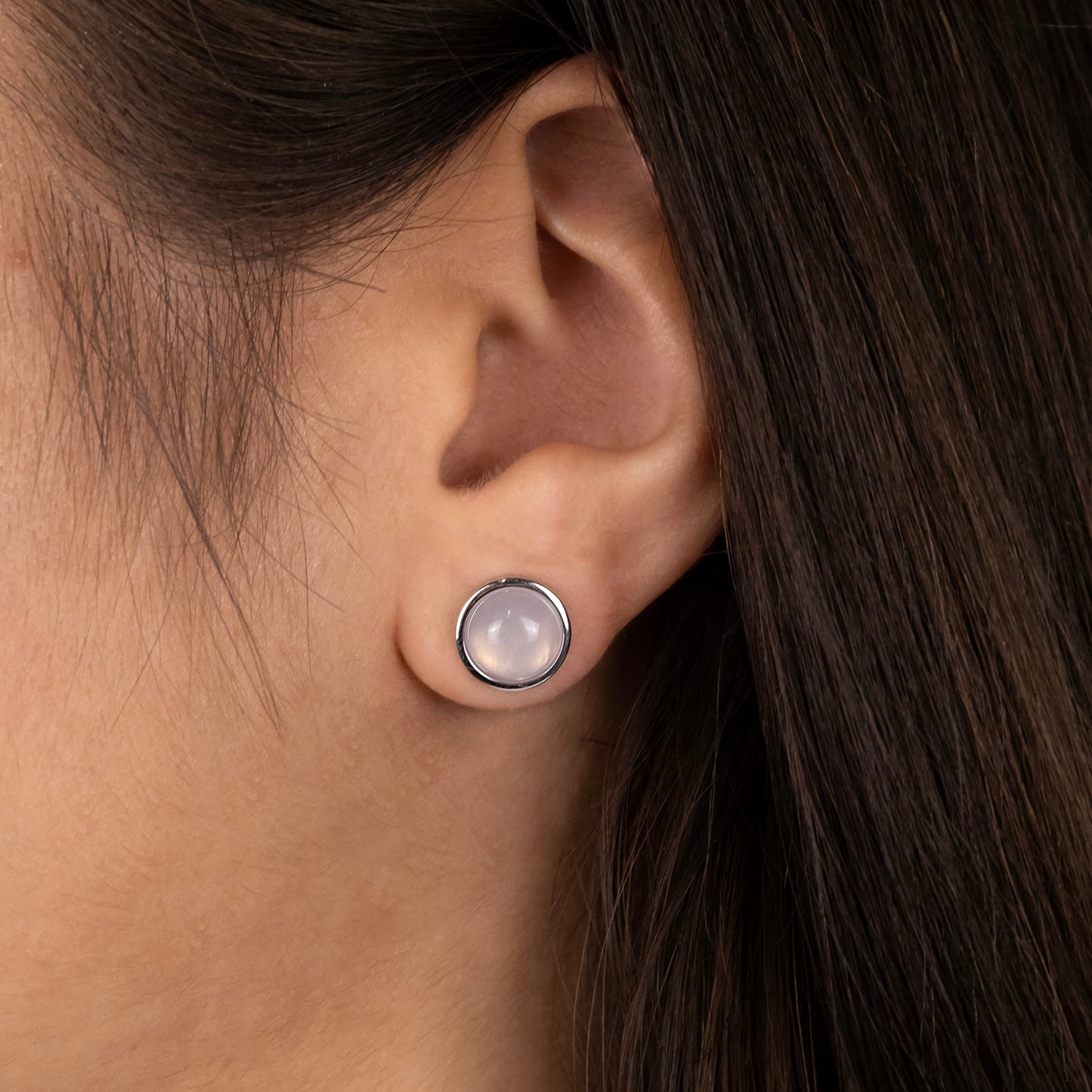 Seitenansicht einer Frau mit braunen Haaren, die einen silbernen Ohrstecker mit Rosenquarz aus der Powerful Stone Kollektion trägt.